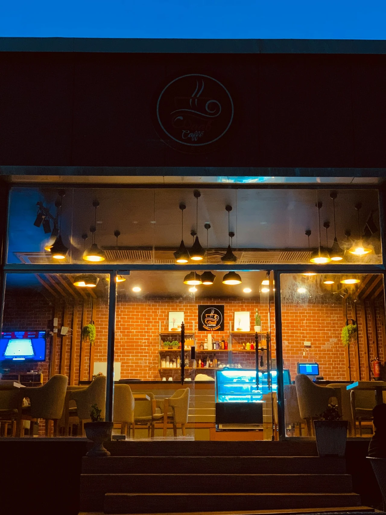 A warmly lit cafÃ© exterior with a glowing entrance at dusk.
