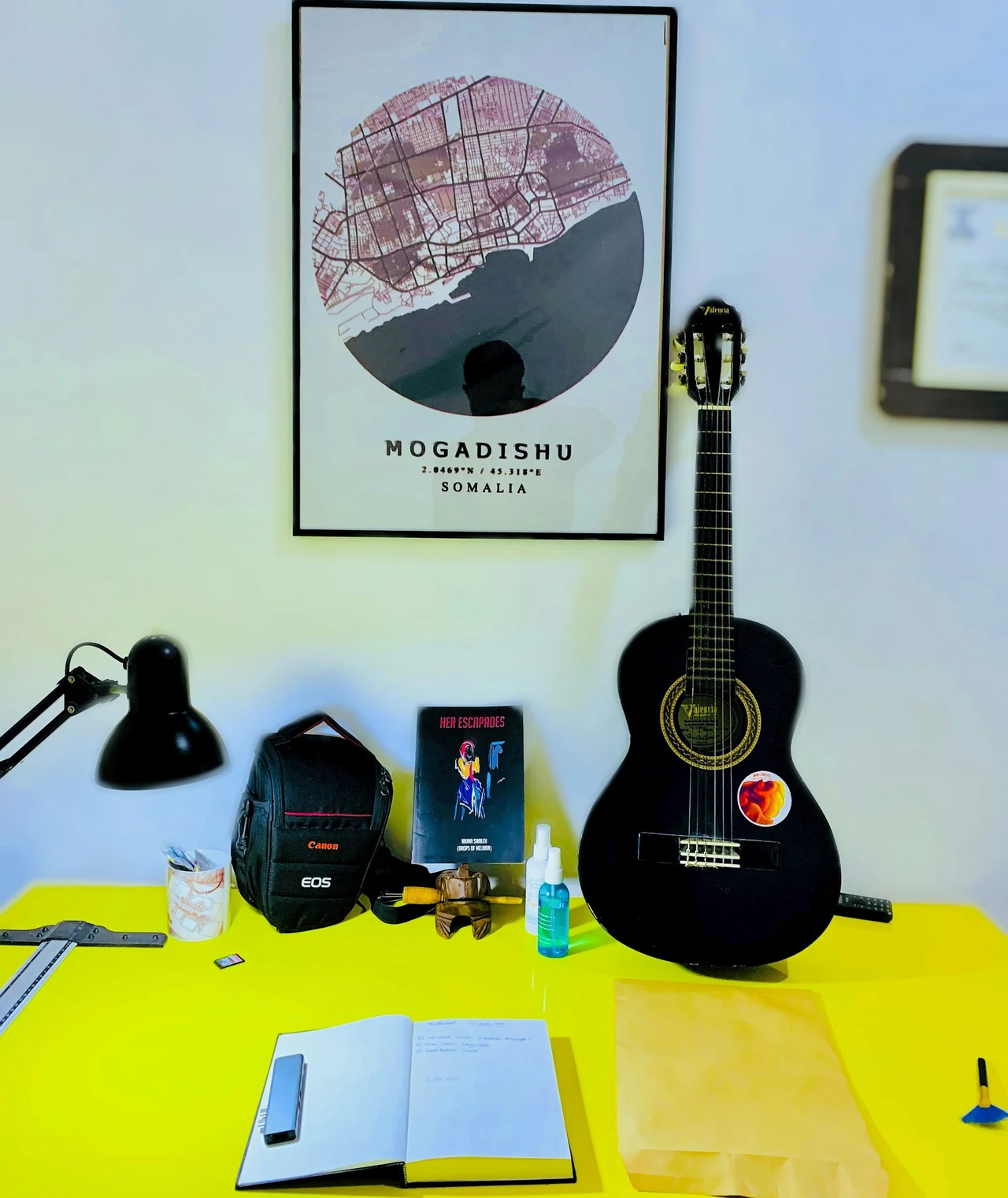 A guitar, headphones and desk objects beneath a Mogadishu poster.