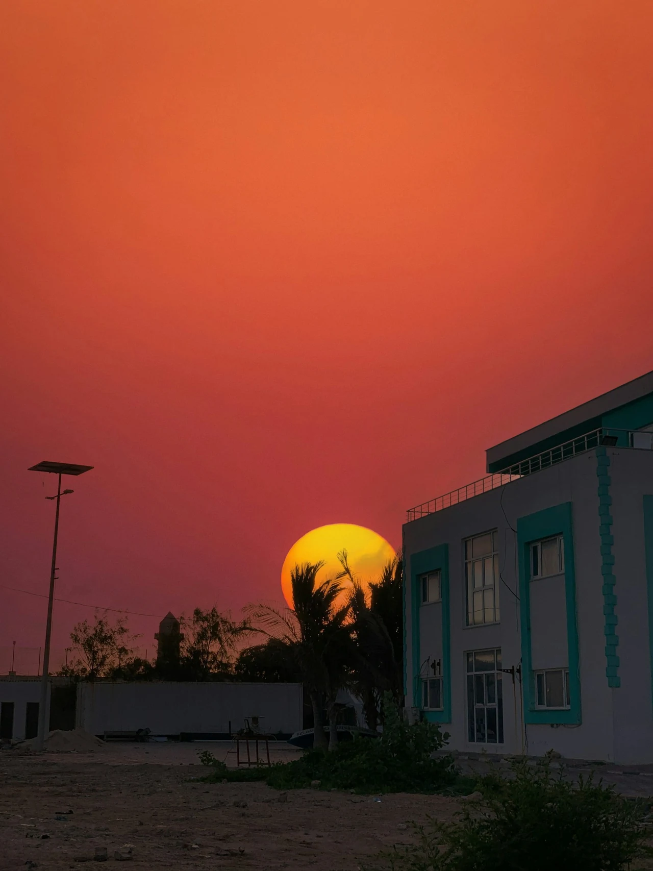 A low sun beneath an orange sky beside a building.