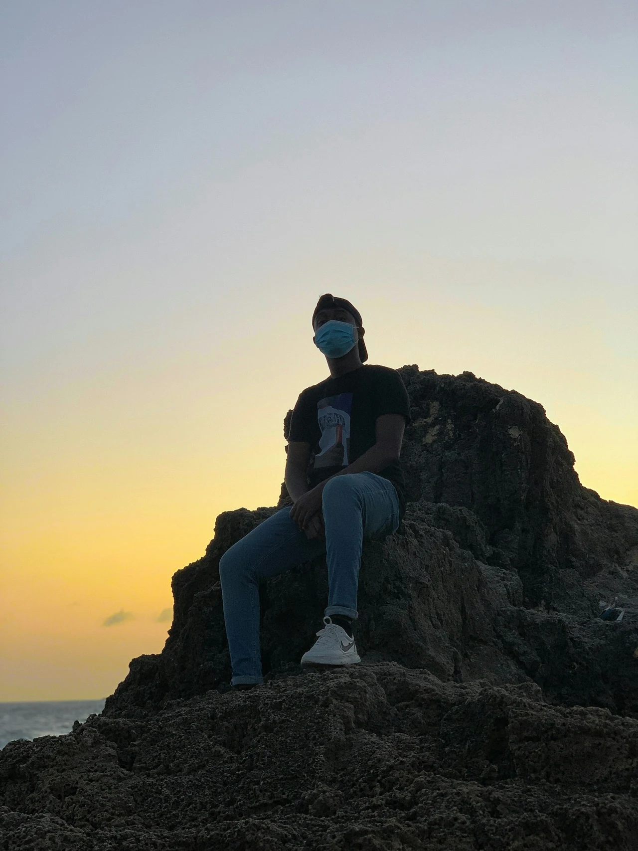 A person sitting on rocks against a softly lit evening sky.