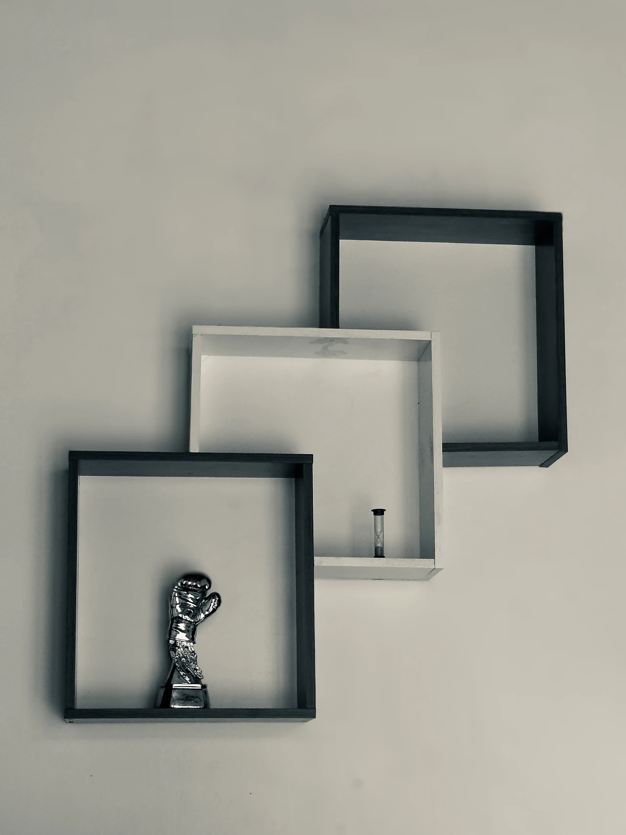 Three overlapping wall shelves holding a boxing-glove trophy and a small hourglass.