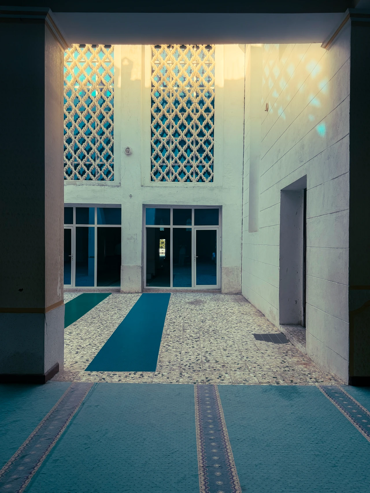 Sunlight passing through patterned screens above blue prayer carpets.