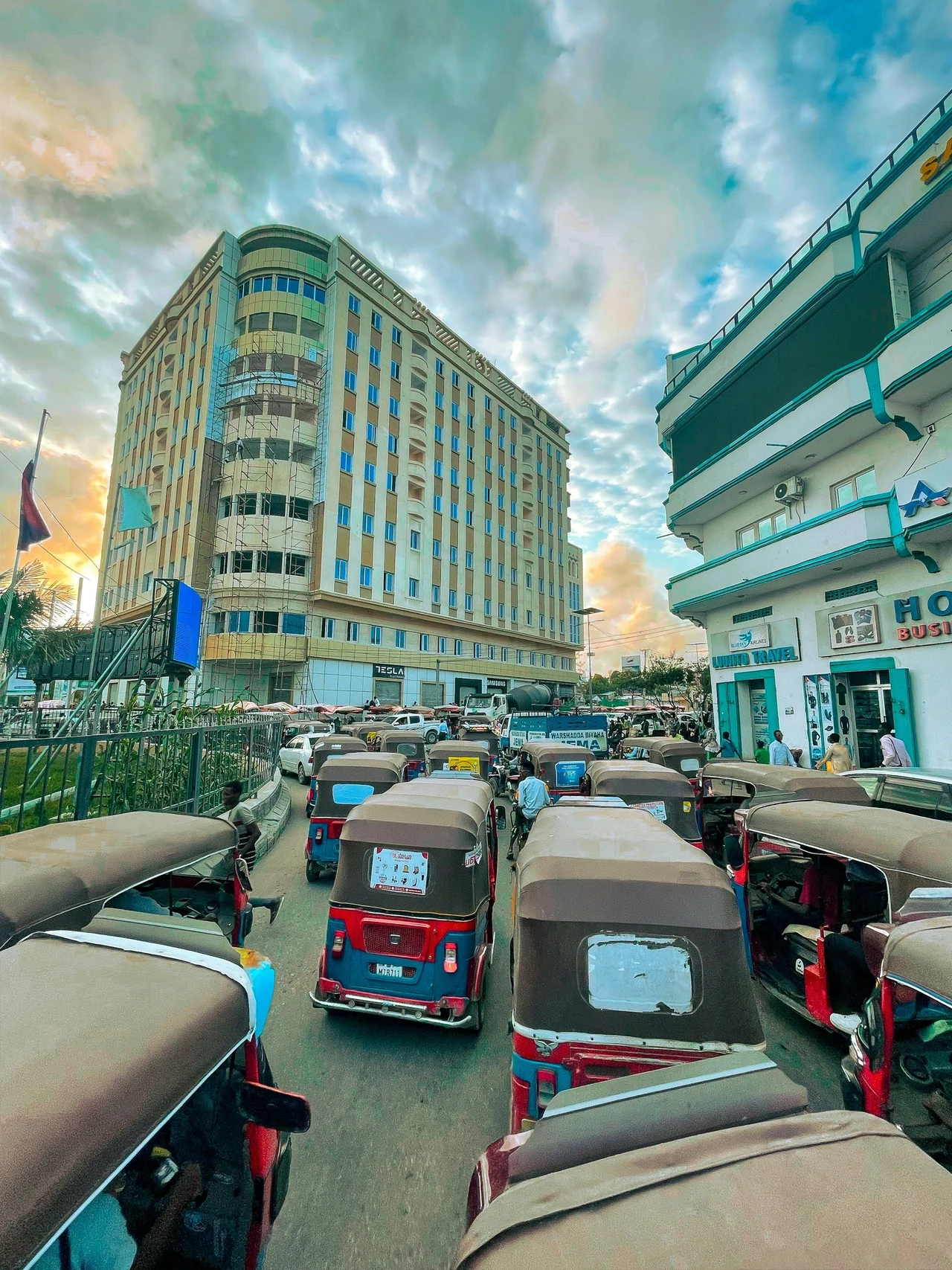 A busy street with vehicles and a tall building under a blue sky.
