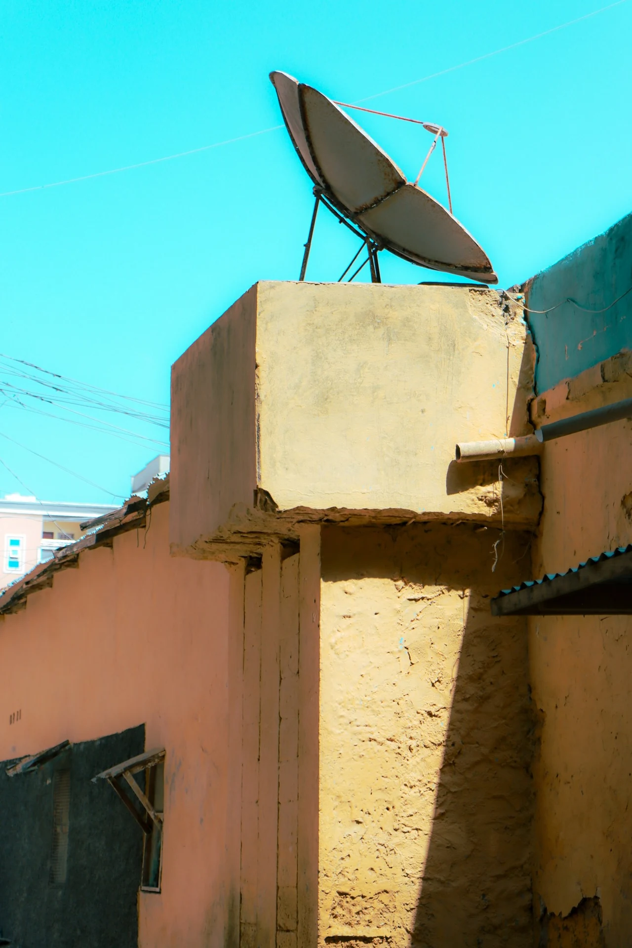 A satellite dish above a sunlit rooftop against a turquoise sky.