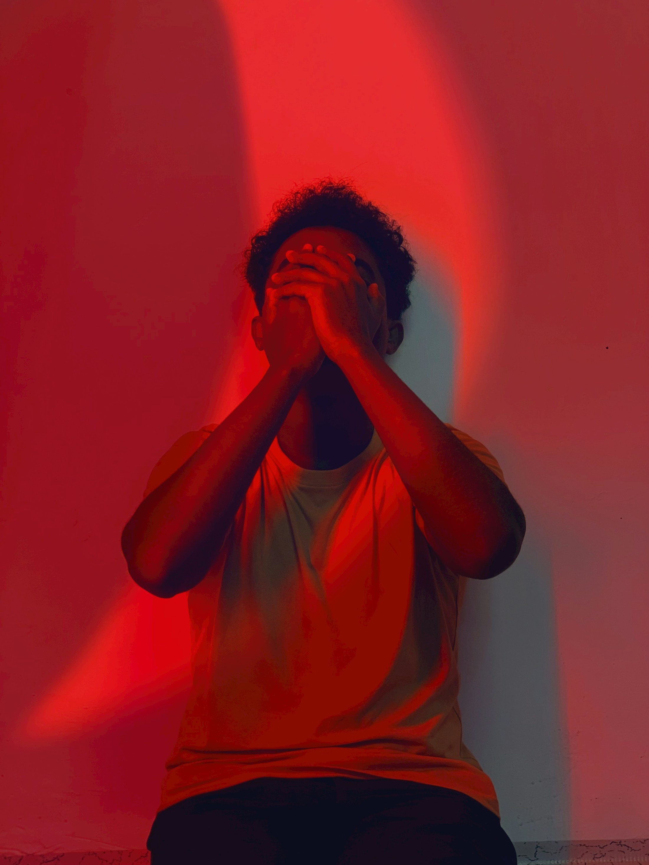 Person covering face with hands under red light.